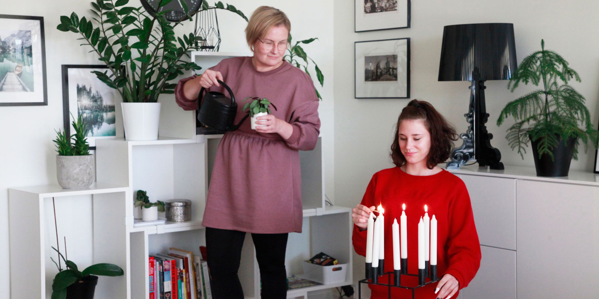 kiertotalous_2000x1000px Äiti ja tytär olohuoneessa, kynttilöitä sytytetään ja kukkia kastellaan.