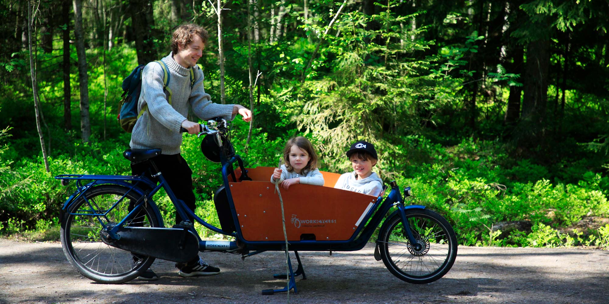 Isä ja lapset pyöräretkellä metsäpolulla.